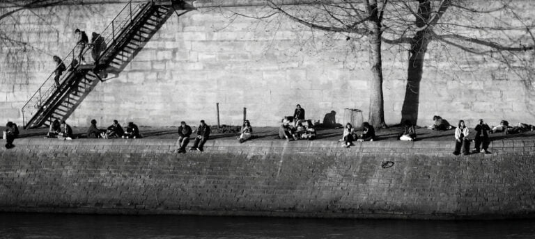 Émotion authentique à Paris : Parisiens baignés de soleil sur les quais de l'île de la Cité. Une capture de l'instant qui incarne l'élégance et l'authenticité par le photographe de Toulouse spécialisé dans les mariages chics.