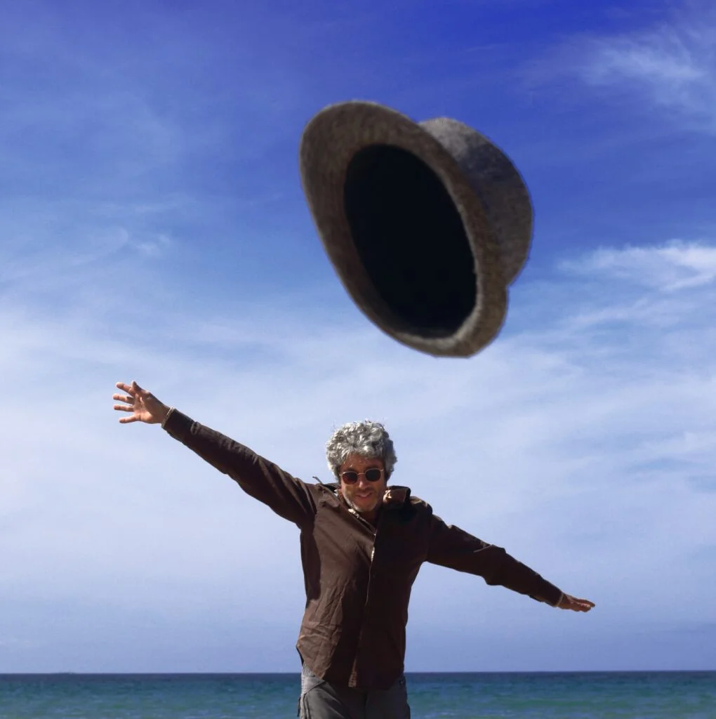 Autoportrait de Manuel VELASQUEZ VZ, photographe de mariage à Toulouse, lançant son chapeau avec énergie devant la mer, pour des mariés chics basé à Toulouse en Haute Garonne.
