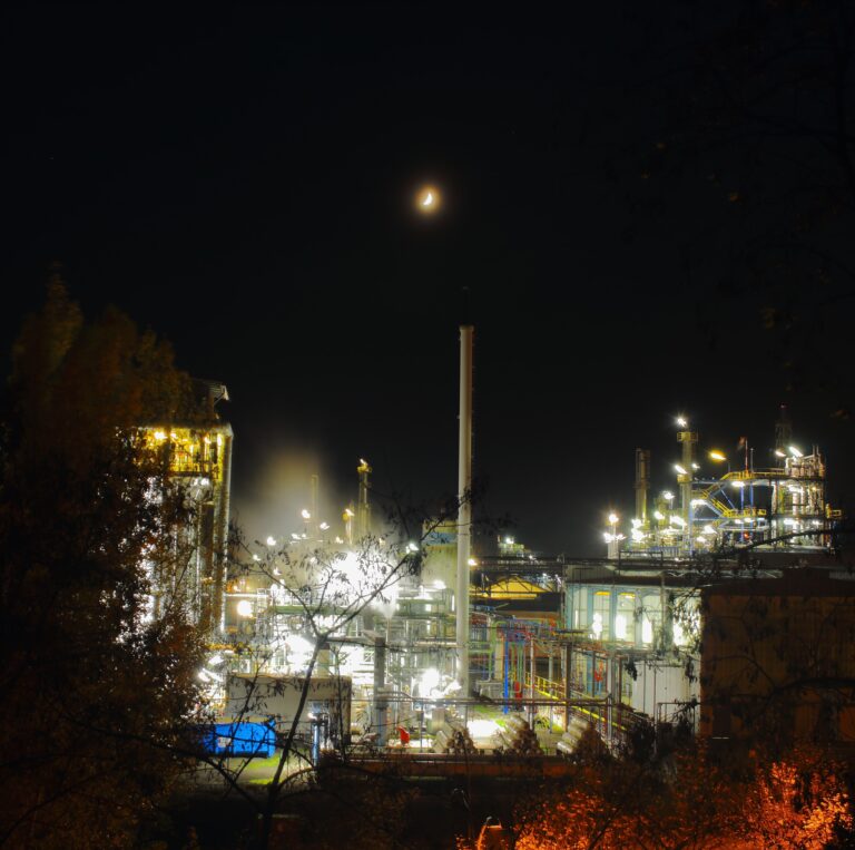 Nocturne industriel : Image d'une usine la nuit, sous un croissant de lune, avec une cheminée à Boussens. Une perspective unique capturée par le photographe, ajoutant une touche d'atmosphère à votre expérience visuelle.