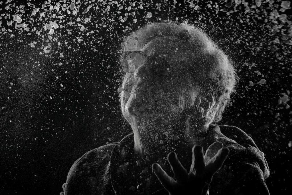 Portrait en noir et blanc d’Hélène, 81 ans, recouverte de farine, les mains levées dans un geste de défi ou de transmission. La farine symbolise l’âme, la mémoire et l’éphémère, thèmes centraux du projet 'Je suis vieux et je t'emmerde' par Manuel VZ