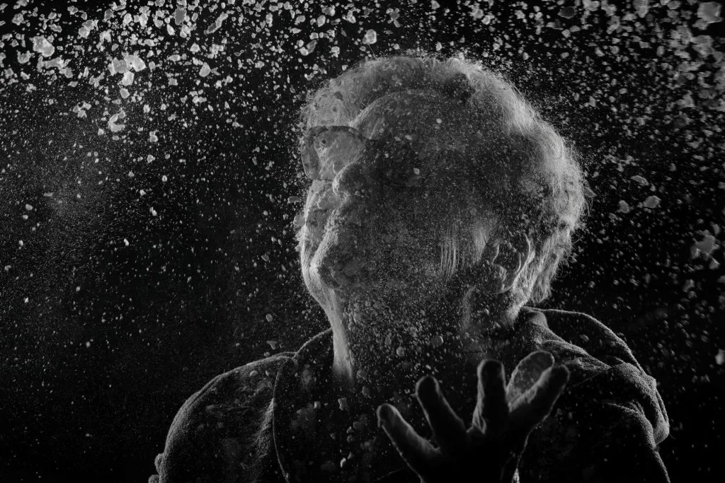 Portrait en noir et blanc d’Hélène, 81 ans, recouverte de farine, les mains levées dans un geste de défi ou de transmission. La farine symbolise l’âme, la mémoire et l’éphémère, thèmes centraux du projet 'Je suis vieux et je t'emmerde' par Manuel VZ