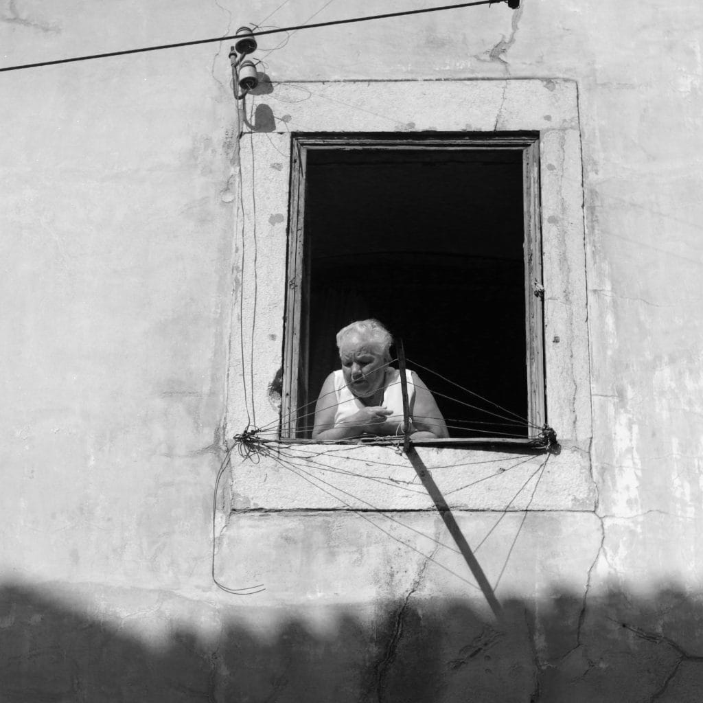 Femme âgée à la fenêtre, entourée de fils électriques, série Silhouettes des Présents Absents, photographie en noir et blanc de Manuel VZ